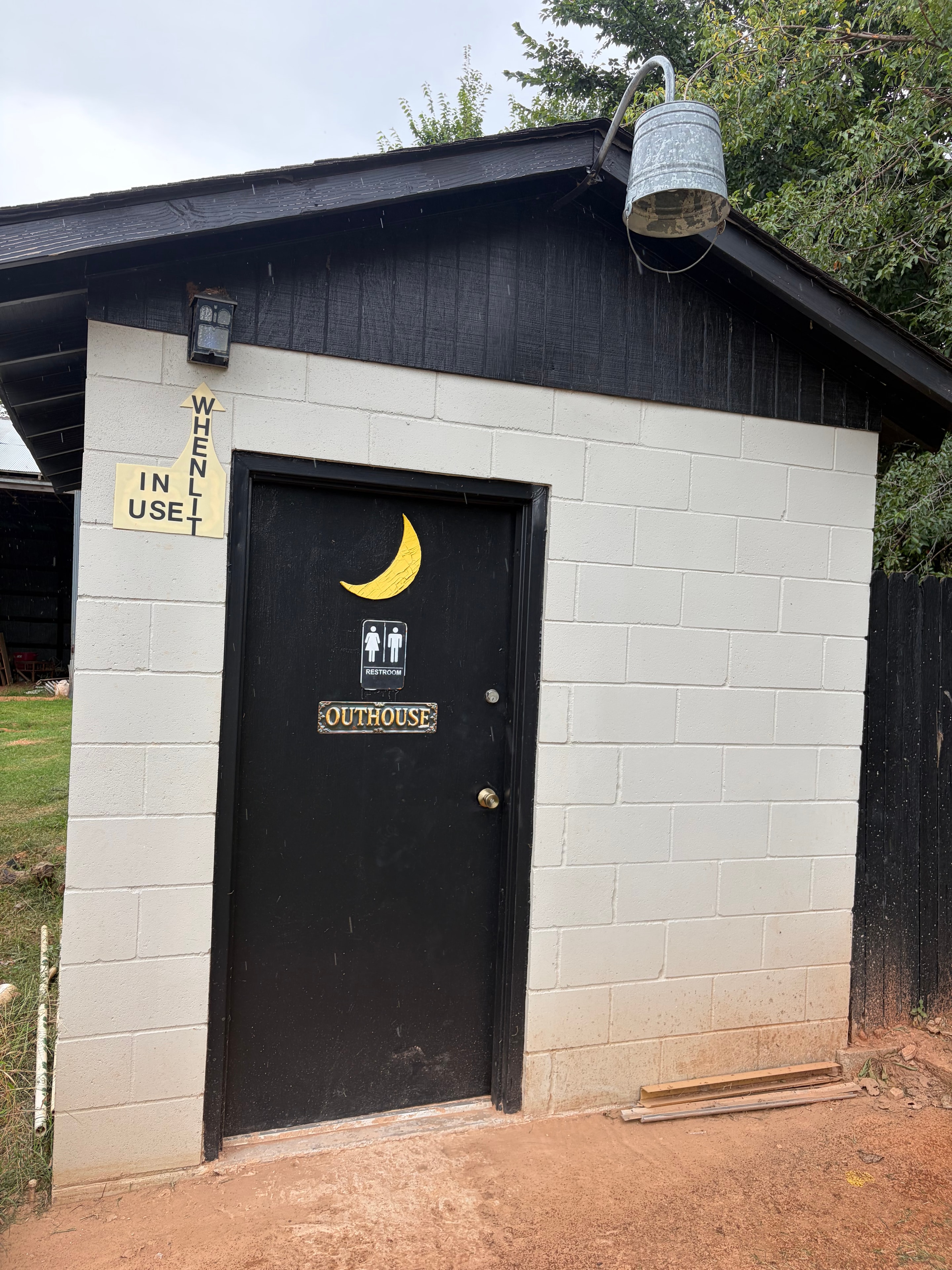 Outdoor restroom building with black door and Outhouse sign