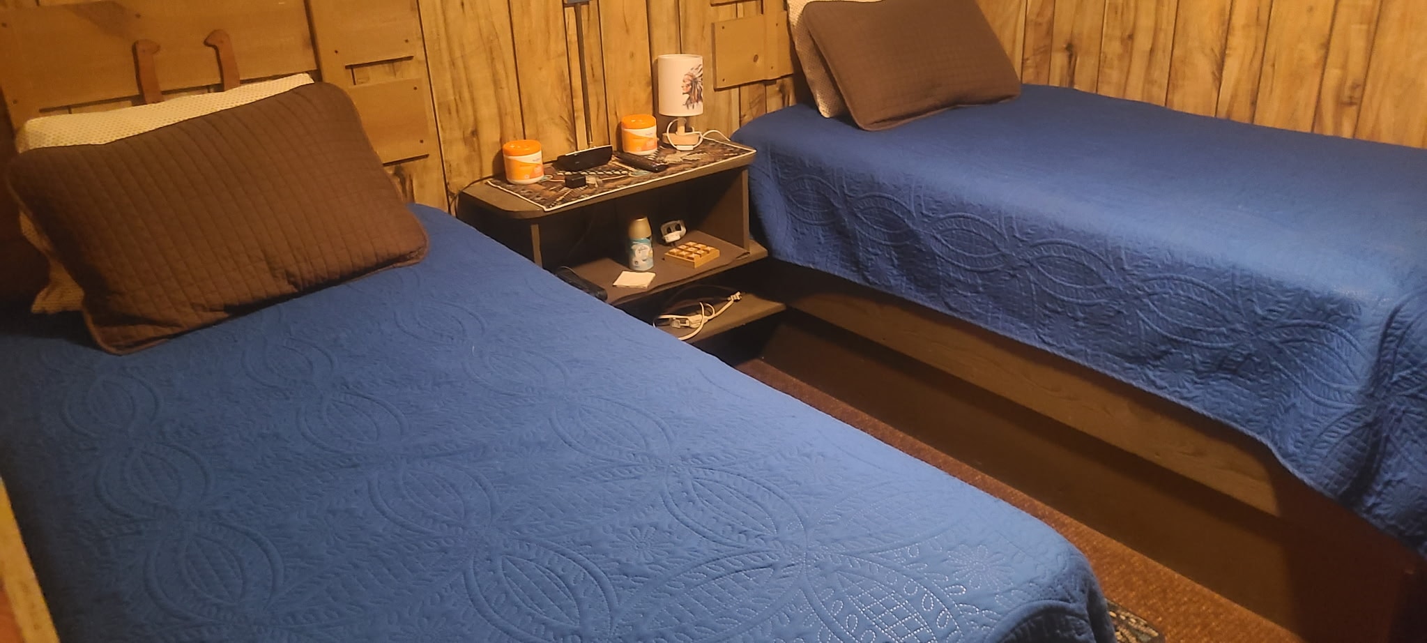 Twin room with two blue-quilted beds and wooden walls